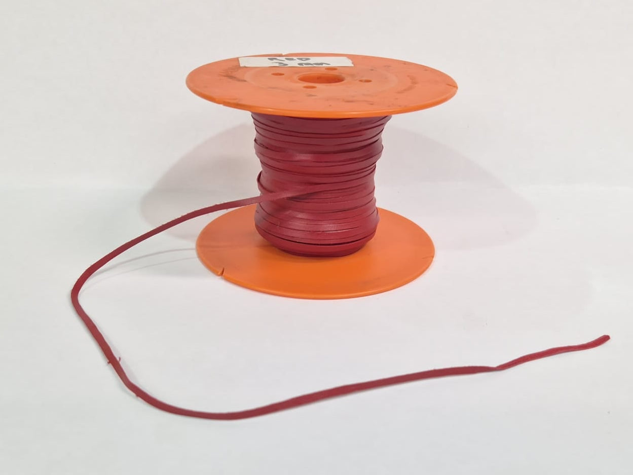 A spool of red leather lace with an orange plastic core, sitting on a white surface against a white background.